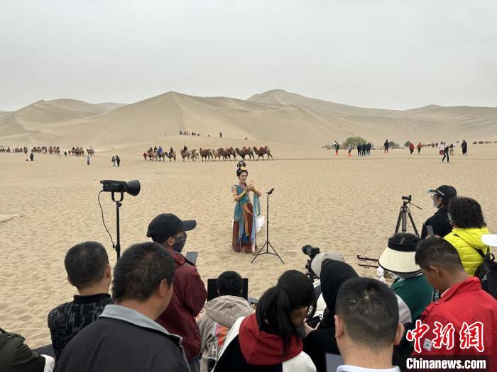 圖為2023年4月底，敦煌大漠“逐舞者”奧楠在鳴沙山月牙泉景區(qū)視頻直播，吸引游人圍觀?！●T志軍 攝